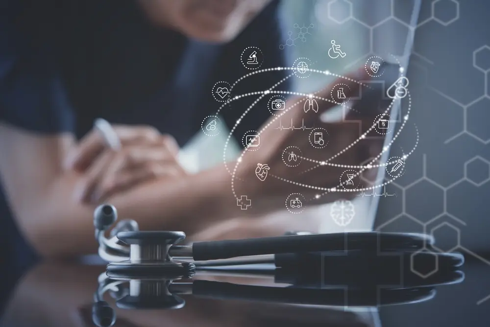 A stethoscope lies in the foreground with a blurred healthcare professional in the background using a laptop, surrounded by a glowing digital network of medical icons including a heart, lungs, brain, and microscope.
